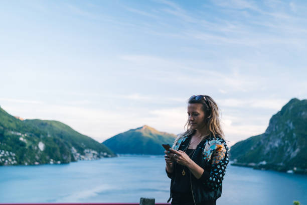 istock Young woman texts on cellphone from lakefront viewpoint 1320993036