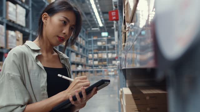 Attractive young Asia businesswoman manager looking for goods using digital tablet checking inventory levels standing in retail shopping center.