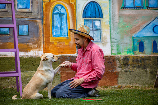 One young man artist playing with his pet outside in the yard on the grass with mural in the background