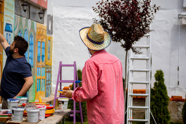 Photo of a group of two male artist painting mural on the wall outside on a sunny day