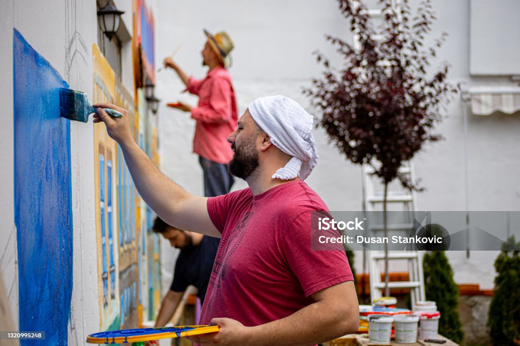 Group of artist painting wall mural Photo of a group of three male artist painting mural on the wall outside on a sunny day Community Stock Photo