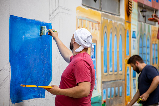 Photo of a group of two male artist painting mural on the wall outside on a sunny day