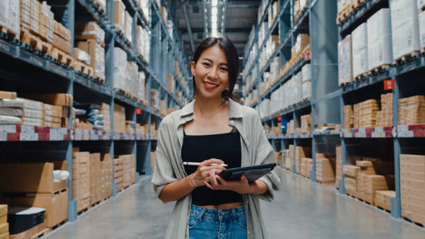 Portrait of attractive young Asia businesswoman manager smiling charmingly looking at camera hold digital tablet stand in retail shopping center. Portrait of attractive young Asia businesswoman manager smiling charmingly looking at camera hold digital tablet stand in retail shopping center. Distribution, Logistics, Packages ready for shipment. storage room stock pictures, royalty-free photos & images