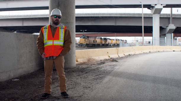 istock Construction worker in full personal protection equipment posed in front of safety barrier with elevated highway and diesel locomotive in background 1320998461
