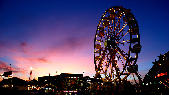 State Fairground Farris Wheel Ride with Multicolored Lights Spinning at Sunset along with Carnival Games, Carnival Rides in image.