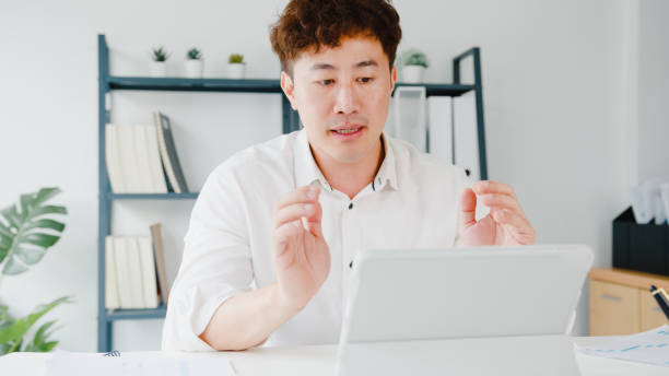 istock Young Asia businessman using tablet talk to colleagues about plan in video call while smart working from home at living room. 1320998608