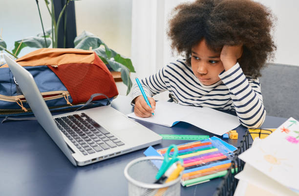 kleine schülerin studiert zu hause und macht ihre schulhausaufgaben, sitzt am tisch mit einem laptop - child thinking writing little girls stock-fotos und bilder