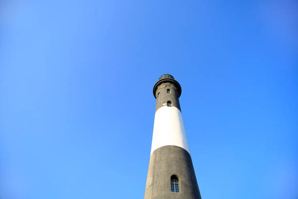 a picture of a Black and white lighthouse on the ocean as the sun is setting