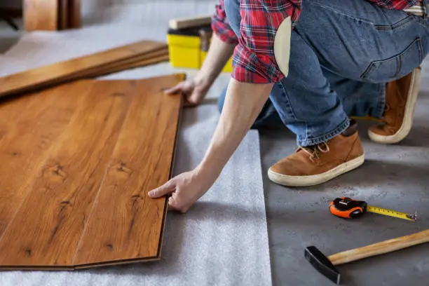 Man worker installing laminate flooring. Wooden laminate floor plank and tools with male hand