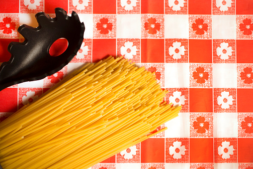 Spaghetti and spaghetti server on kitchen table.  Red Checked table cloth.