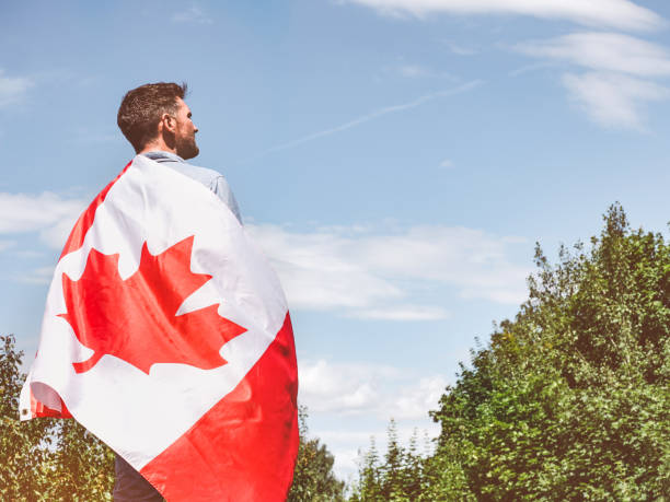 istock Attractive man holding Canadian Flag on blue sky background 1321001058