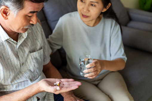 Senior woman giving her husband daily prescription medication in living room at home