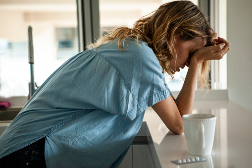 Vista lateral de la mujer adulta media emocionalmente estresada de pie en la cocina junto a una ampolla de píldoras photo