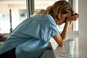Side view of emotionally stressed mid adult woman standing in the kitchen next to a blister of pills
