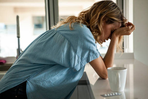 Side view of emotionally stressed mid adult woman standing in the kitchen next to a blister of pills stock photo