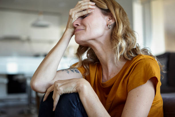 Portrait of crying woman with hands on her face while sitting indoors stock photo