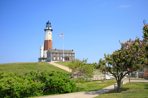a picture of a White lighthouse with brick on the ocean with a green lawn