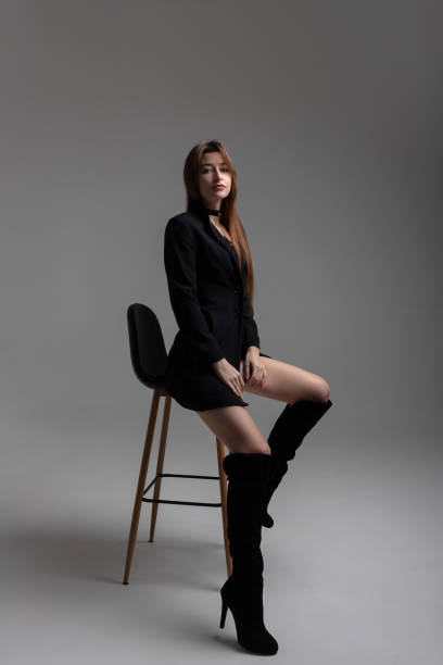 istock Model in total black sitting on bar stool on grey background in studio. Fashion concept. 1321008869