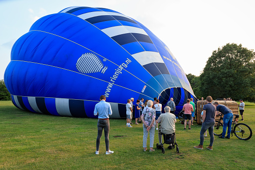 Almelo, Overijssel, Netherlands, june 3rd 2018, a hot-air balloon team is making preparations for an evening flight with a traditional-shaped basket and blue balloon - the balloon has been spread out on the ground and is being inflated with cold air - spectators (passengers, their family and friends) are gathered around the basket - [sequence 04/10]