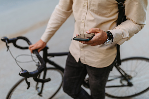 Close up of young businessman using cellphone while commuting to work with his bicycle