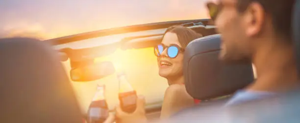 The happy woman sit with friends in a cabrio on the bright sun background