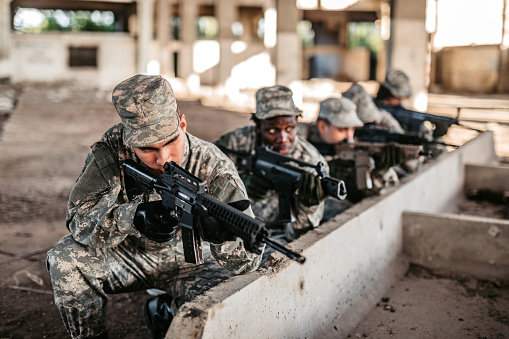 Military assault team taking cover in abandoned building on battlefield.