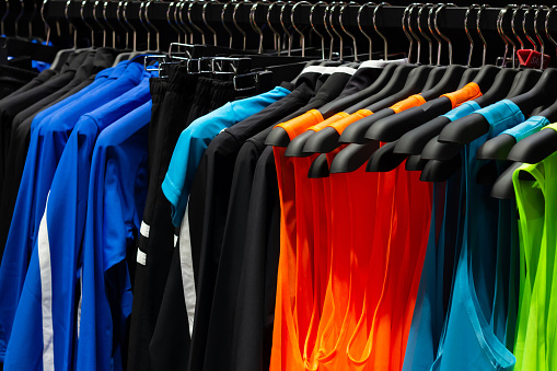 Photo of multicolored sport sleeveless t-shirts and shirts hanging on store rack.