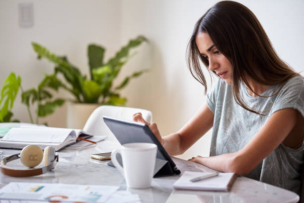 istock Smiling young woman using touchscreen device while holding cup of hot drink during the morning 1321017623