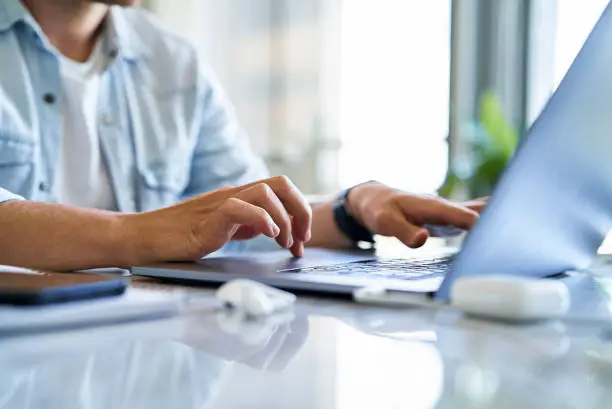 Mid section of young man typing and using laptop while sitting on table at the office