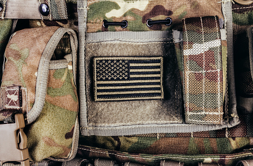 Close-up photo of multi camouflaged soldier vest pouches system with american flag patch.