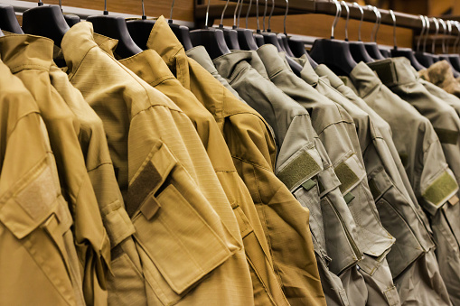 Photo of olive colored military shirts and ripstoprs hanging in military store rack.