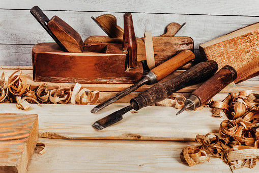 Photo of wooden old fashioned planes with carving chisels laying on workbench table with sawdust.
