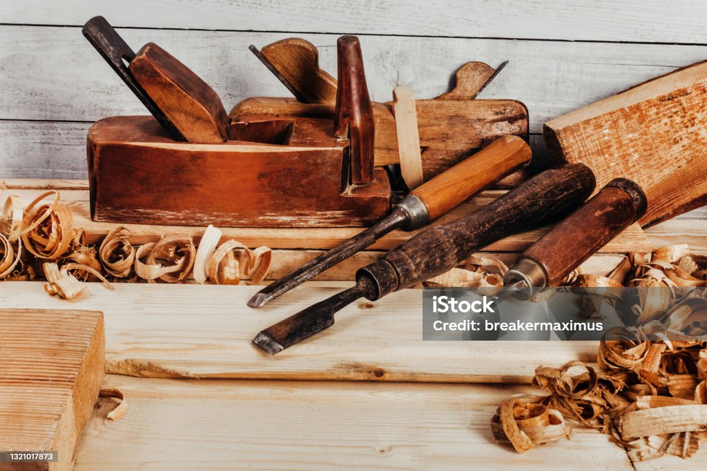 Old fashioned planes with carving chisels laying on workbench table. Photo of wooden old fashioned planes with carving chisels laying on workbench table with sawdust. Carpenter Stock Photo