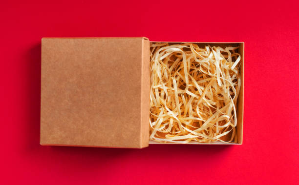 istock Carboard box packaging with sawdust on red background. 1321017903