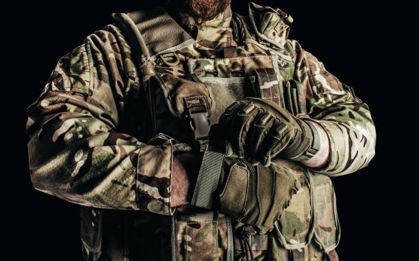 Soldier in level 3 camouflaged armored vest putting on tactical gloves. stock photo
