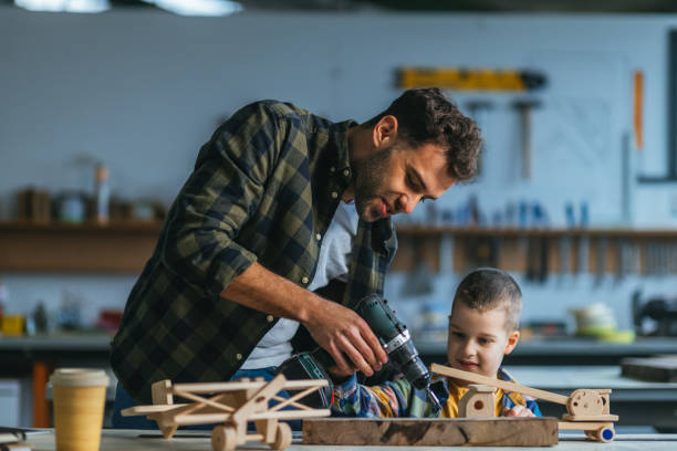 istock Little boy and dad in carpenter workshop making wooden toy 1321019072