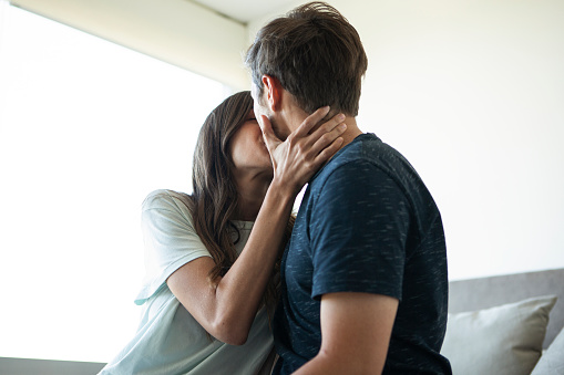 Woman and man kissing while sitting in the bedroom during daytime
