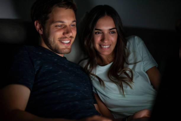 istock Smiling couple lying on bed next to each other while watching online content during nightime 1321019833