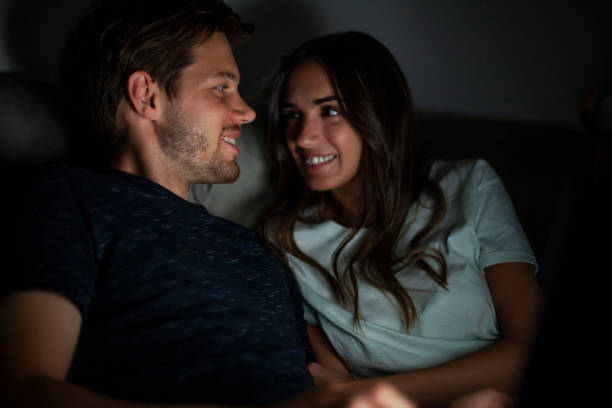 istock Smiling couple lying on bed face to face while watching a movie during nightime 1321019862