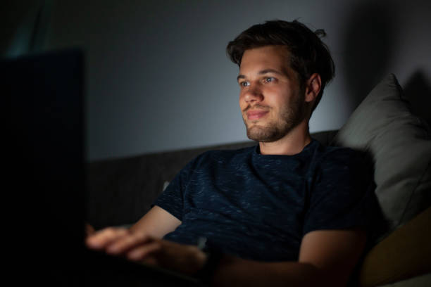istock Portrait of young man typing on laptop while sitting on sofa during nightime 1321019874