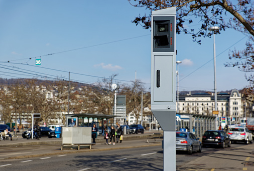 stationary radar speed camera camera in big city with cars and people in blurred background, speed controls are important to ensure traffic safety, daytime, sunset, image is strongly focused on the radar