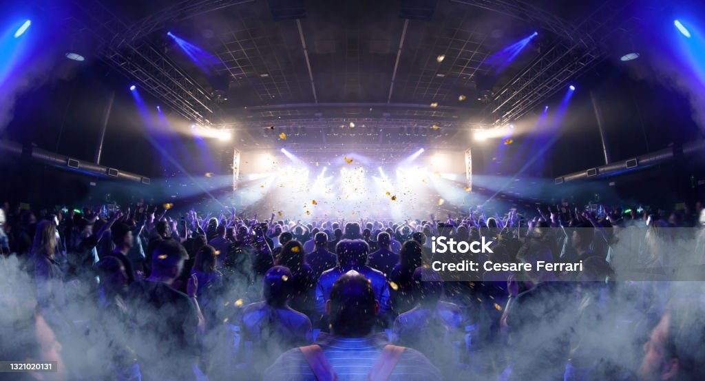 Concert crowd venue Concert crowd inside a venue, lens flare and smoke are visible. Performance Stock Photo
