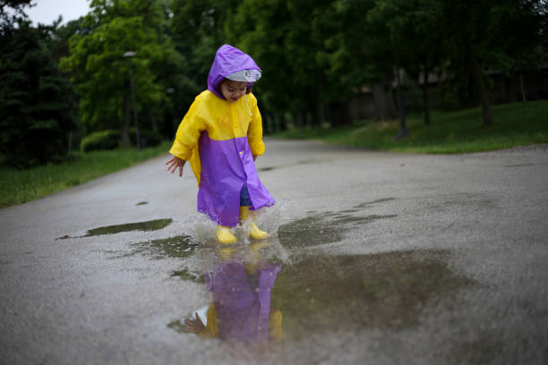 ребенок в желтых сапогах прыгает в лужах. фондовый фото - child looking messy urban scene стоковые фото и изображения