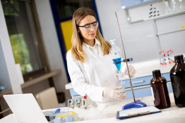 Photo of Young female researcher working with blue liquid at separatory funnel