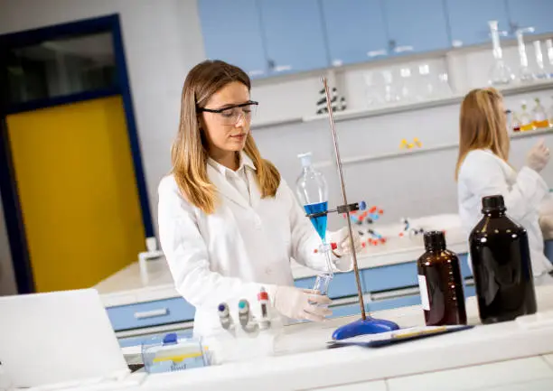 Photo of Young female researcher working with blue liquid at separatory funnel