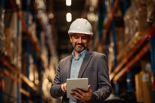 Manager with safety helmet holding digital tablet in warehouse