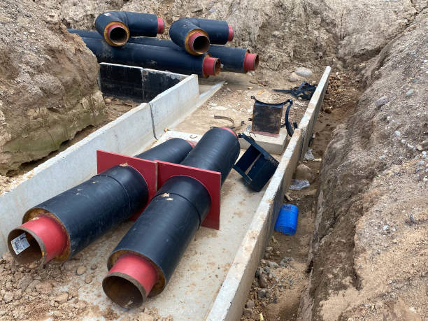 laying of underground storm sewer pipes at the construction site. installation of water main and sanitary sewer on background tower cranes and blue sky. ground water drainage system pipes - order repairing telephone change imagens e fotografias de stock
