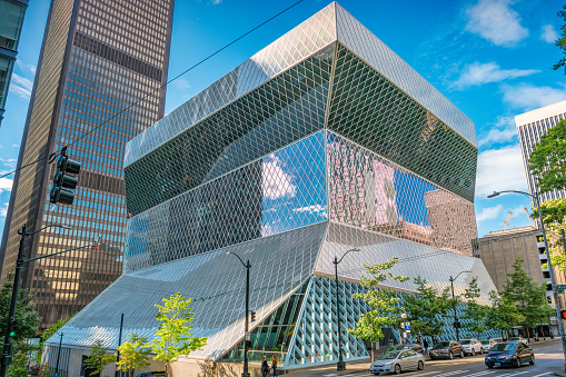 Pedestrians stand in front of the Seattle Central Library in downtown Seattle Washington USA on a sunny day.