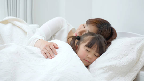 ベッドの中で若いアジアの母と娘 - 睡眠 ストックフォトと画像