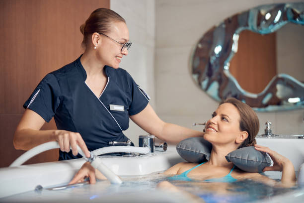 Contented lady receiving an underwater shower massage Young female therapist smiling at her patient during the hydrotherapy procedure in a spa salon hydrotherapy stock pictures, royalty-free photos & images